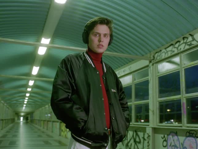 Man wearing headphones stands inside graffiti covered pedestrian bridge at night