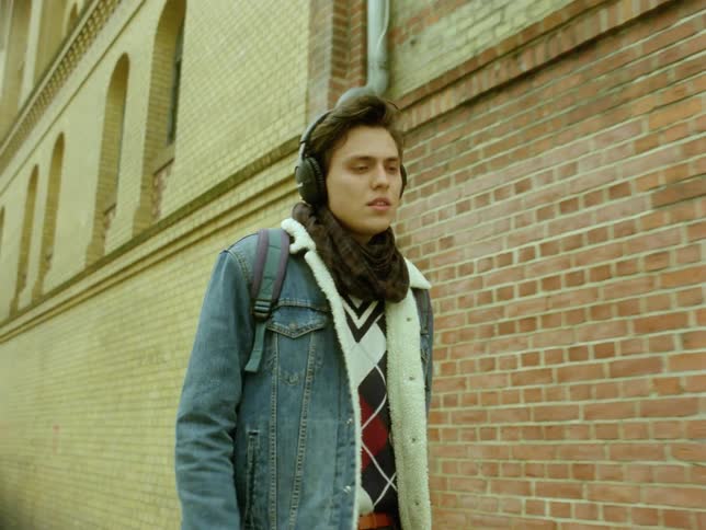 Young man walking along the city sidewalk with headphones