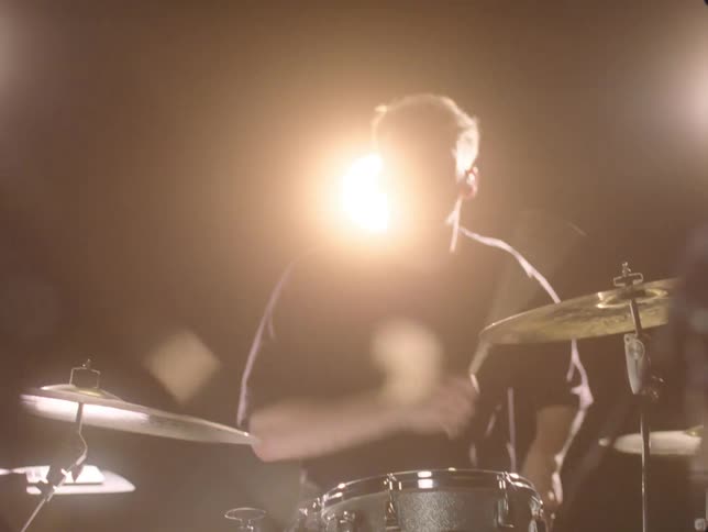 Drummer plays drums while performing with his band under bright spotlights