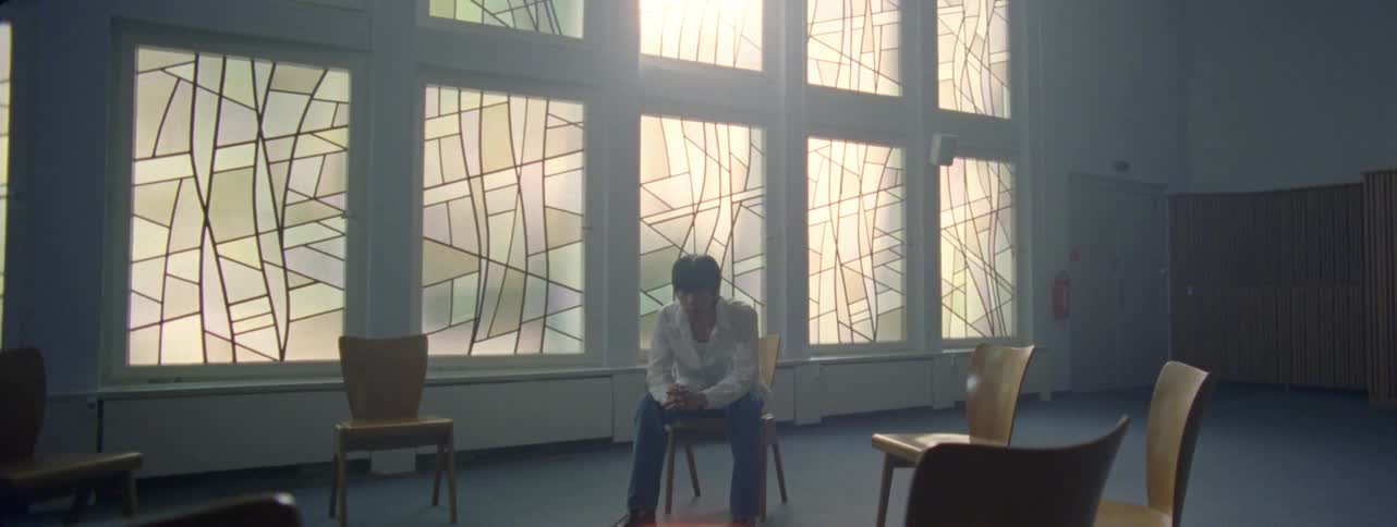 Several empty chairs are arranged in a circle a young man sits in one of them