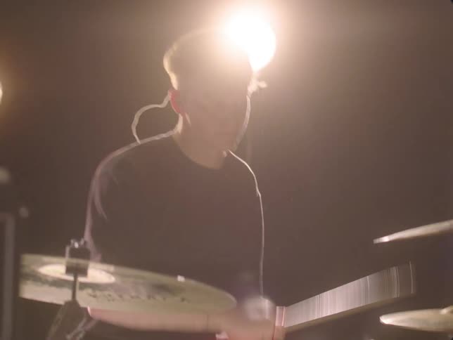 Three adults play guitars and a drum set in a band