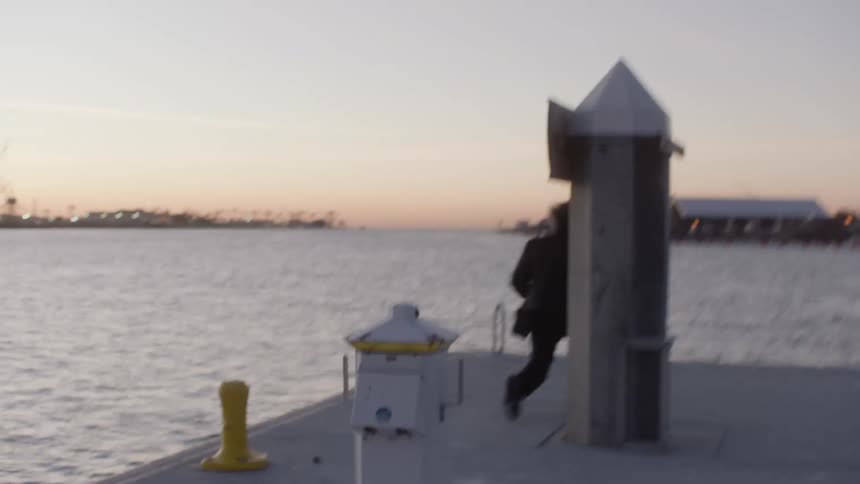 A sad man in a suit runs up to the end of a pier at sunset
