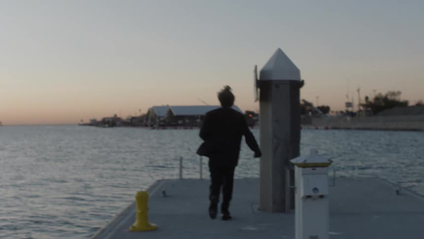 View of a man in a black suit running on a dock and kneeling