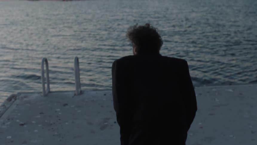 A man kneels by the shore at sunrise