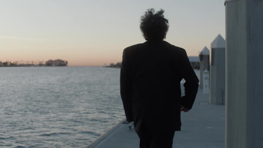 Back view of a man running on the seaside dock in a black blazer