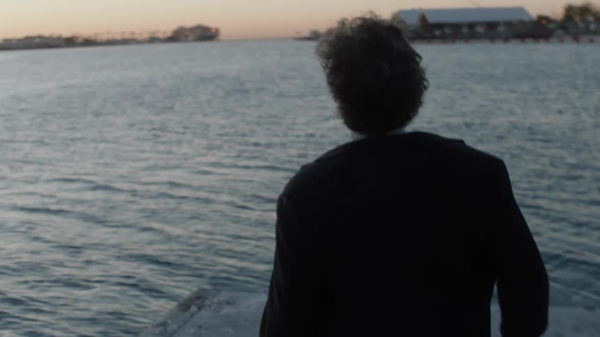 View of a man with his back walking desolately and kneeling on the seaside pier one morning