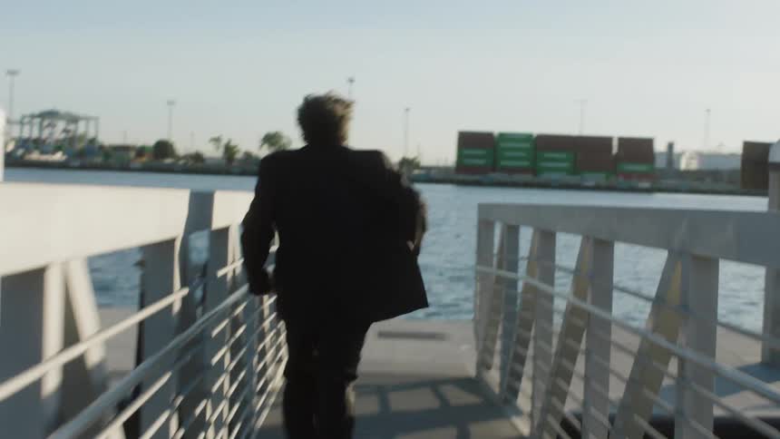 Back view of a man in a black suit running on a seaside dock