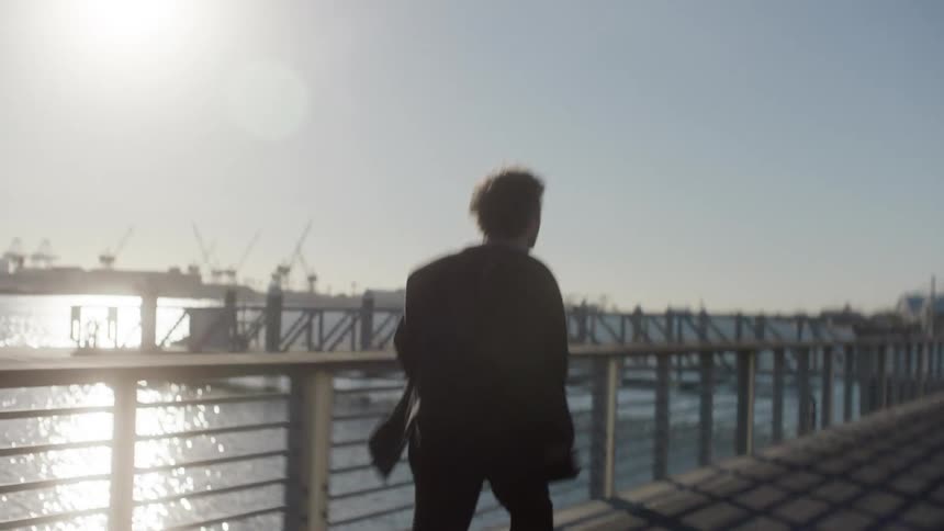 Back view of a man running on a seaside dock while wearing a black suit