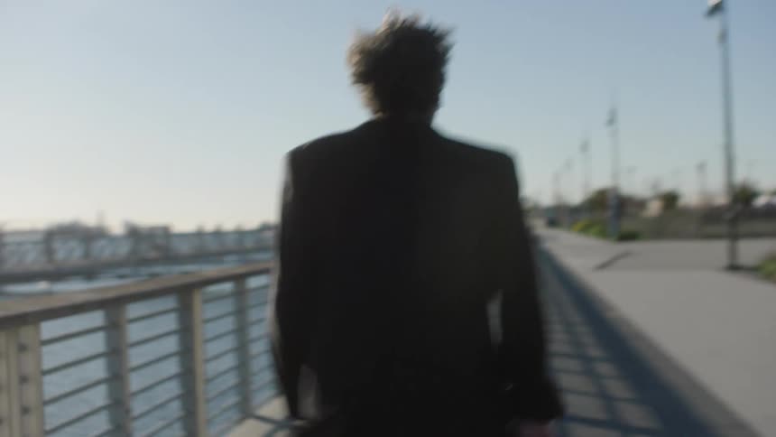 Man with his back turned and in a blazer running on the sidewalk by the sea