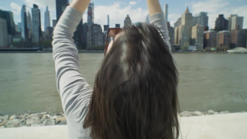 A woman raises her arms in front of the skyline
