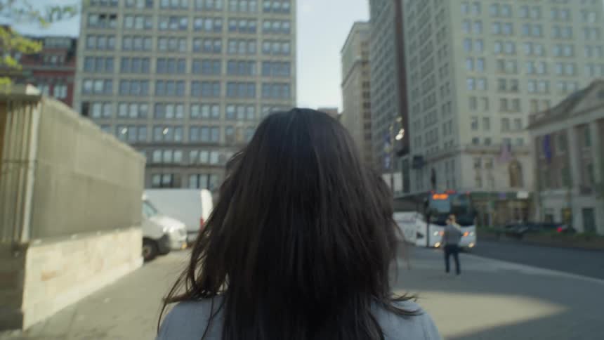 A woman is walking on the sidewalk in the city