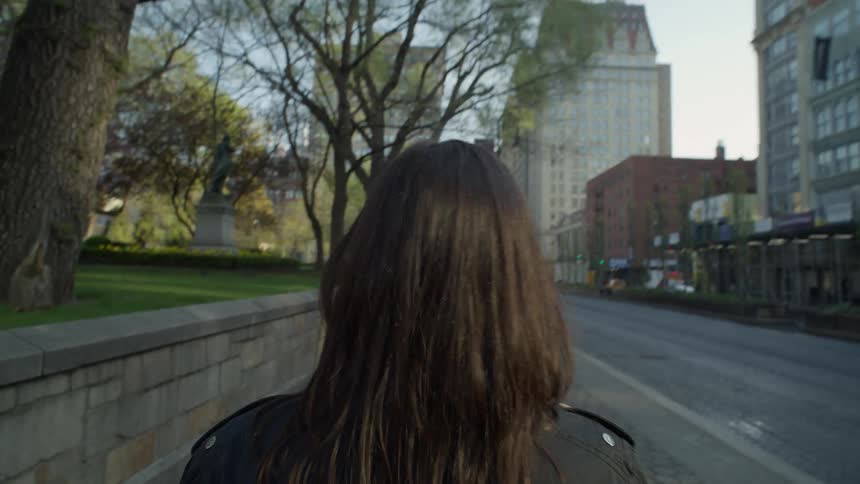 Point of view of a woman with black hair walking on the sidewalk of a metropolis next to a street with vehicle traffic