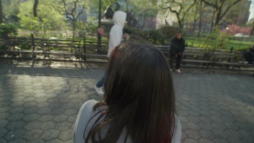 A young woman drinks a cup of coffee while sitting on a park bench