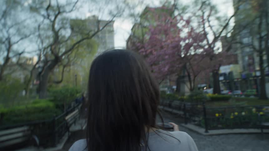 A woman walks through a downtown park in the morning while drinking a coffee