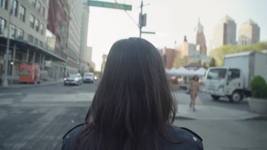 A woman with dark wavy hair strides confidently through the bustling downtown area