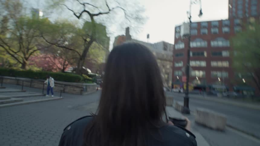 Point of view of a woman holding a cup of coffee and walking on the sidewalk of a metropolis