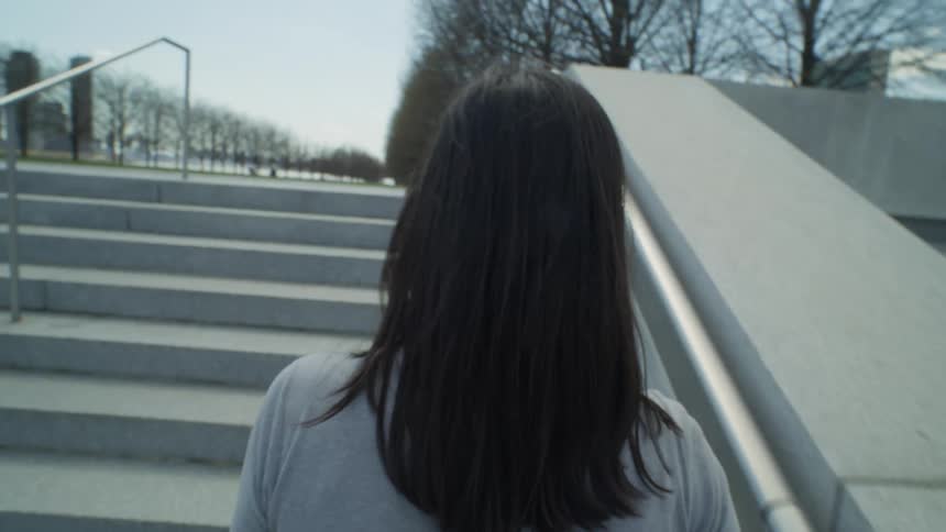 Point of view of a blackhaired woman walking up the stairs towards the park through the city