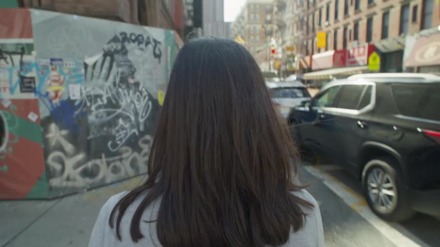 A woman strolls down a bustling city street in the middle of the day