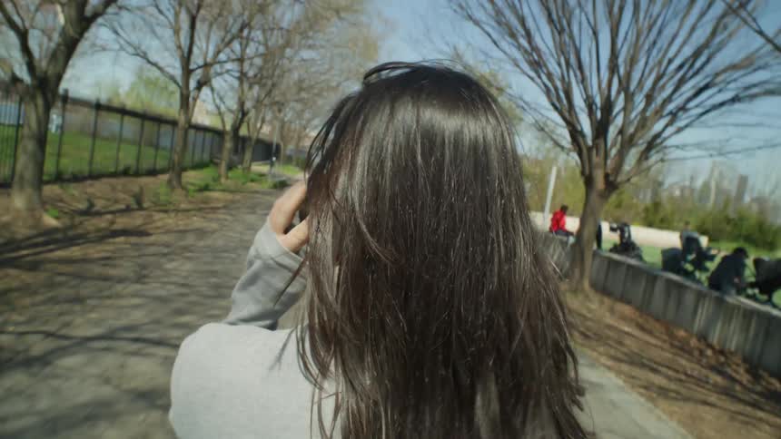 A woman talks on a smartphone while walking through a park