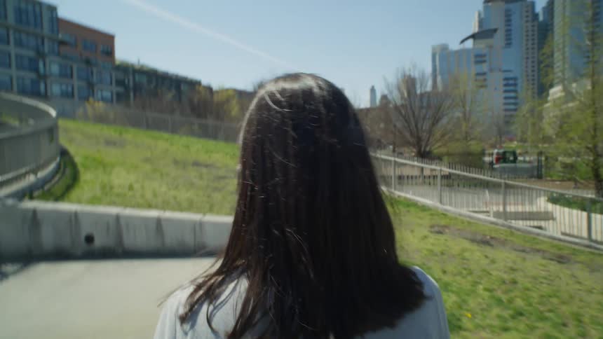 A woman with dark wavy hair and a white shirt strolls in the green park