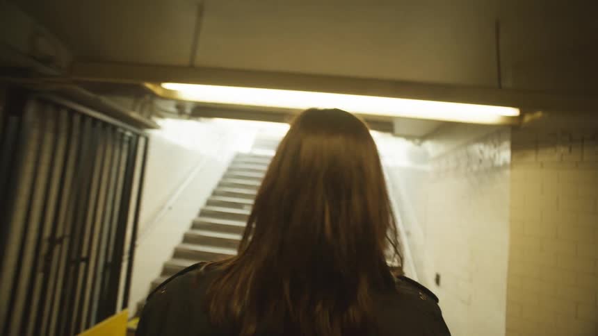 Black haired woman walking towards a staircase and going up from a subway station