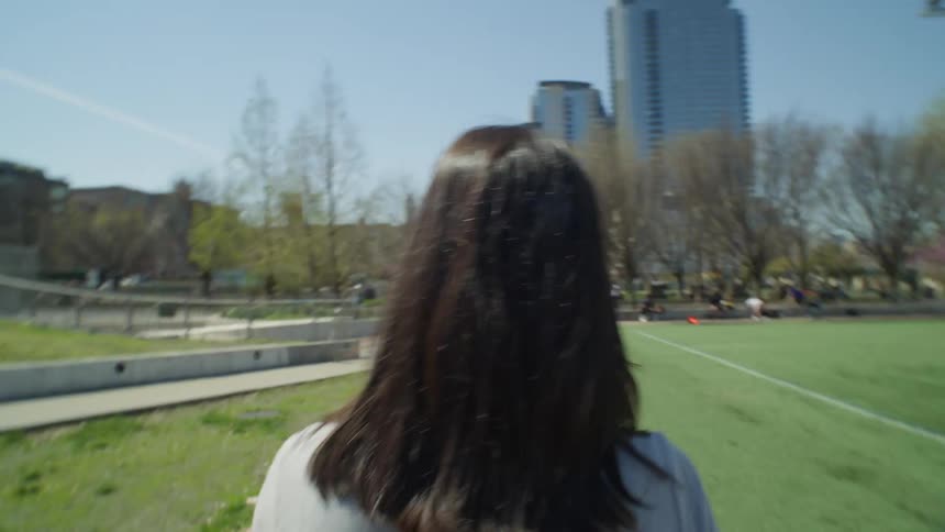 A woman walks by a soccer field in a park and claps her hands