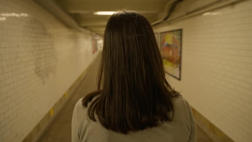 Perspective of a woman seen from behind walking down a train station corridor