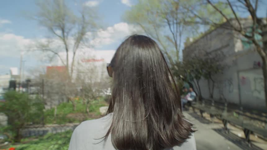 A woman walks through a park and out a gate to a street