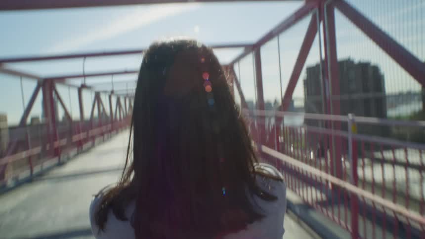Perspective of a woman seen from behind walking on an overpass in a metropolis in daylight