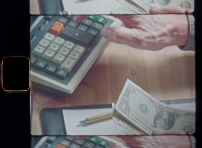 Person using an old electrical calculator computer with keys and display and handling banknotes in his left hand after taking notes on the white paper of his notepad on vintage 8mm film with a nostalgic vibe