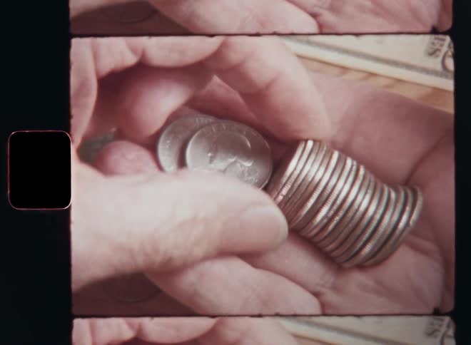 Vintage Super 8mm closeup of old wrinkled hands holding a stack of silver US dollar cent coins and counting the money with his fingers to check the finance status of the household while doing the bookkeeping