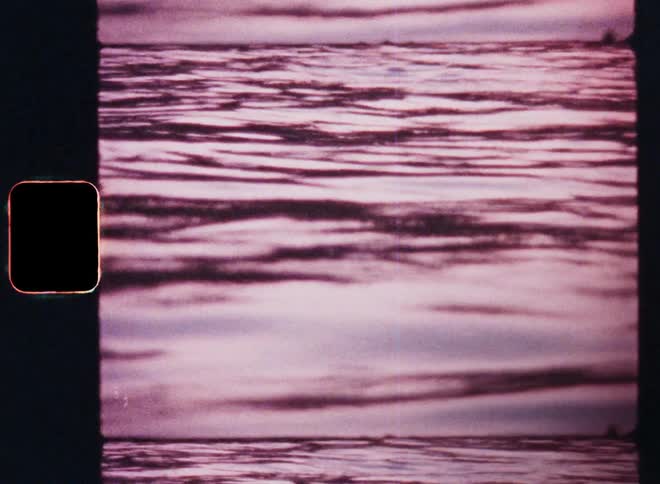 Water waves cause ripples and movement caught on vintage Super 8 film looking like an abstract moving texture with shadows and pink light reflections from the vibrant evening sky