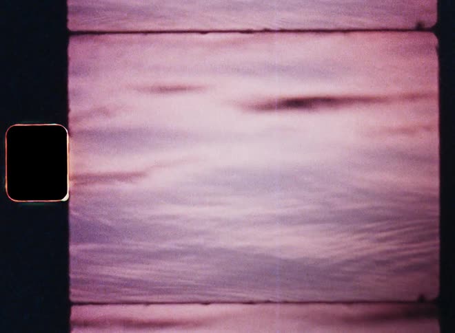 Close up of a body of water reflecting red sky at dusk while rain drops are dripping onto the moving surface of the lake or sea as small waves make the water ripple and move in a dynamic way