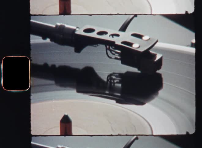 Retro Super8 closeup with upward vertical camera movement of the needle arm of a vintage vinyl record player as a song or music is being played on an old stereo system with authentic film burn