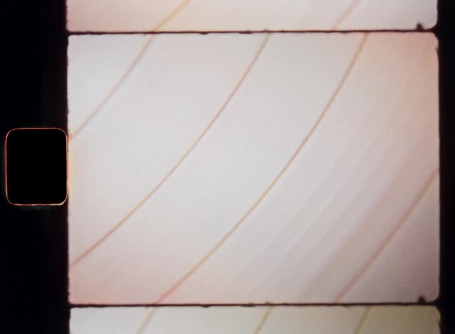 Old Super-8 film footage closeup of a multicoloured vinyl record or a bright colourful disc object with rotating fissures or lines spinning and causing a flicker and shimmering retro effect due to the light reflective surface and rotation movement