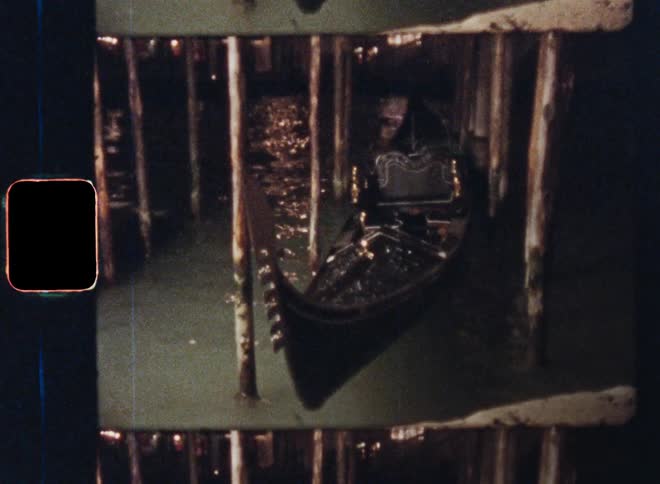 Vintage canoe or Venetian gondola tied up to wooden posts while moving in the waves in the water below a wooden deck or bridge at night illuminated by a headlight or spotlight
