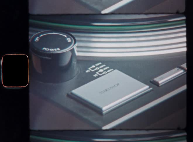 Super 8 close-up of an unrecognizable person that pushes the start or stop button that makes a vinyl record on the turntable spin or it stops the rotation in the end or the finger pressing play or pause on the record player