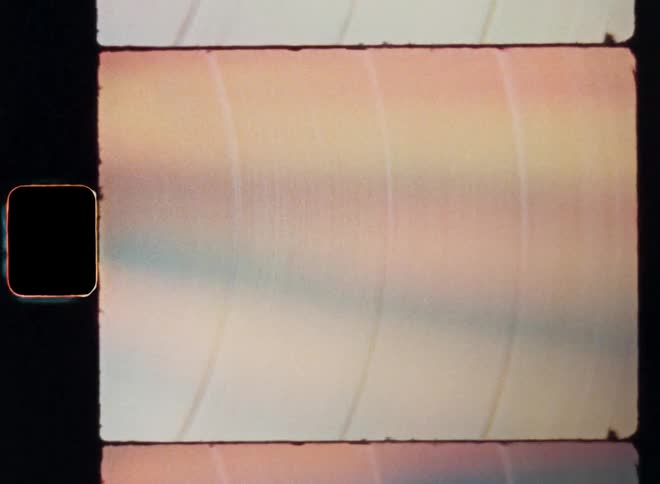 A vibrant vinyl record with bright colors or an abstract colorful multicoloured object with a pink and orange hue is rotating with the moving texture of the shiny reflective surface causing a psychedelic rainbow effect as transition on Super 8 film