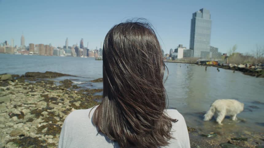 Woman with a white dog looking at the NYC cityscape across the water