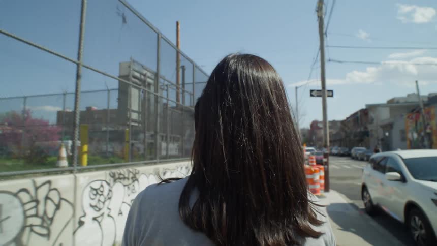 POV of a woman from behind crossing a street in an urban city