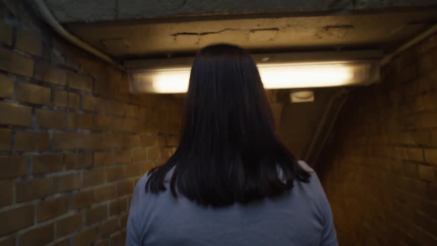 Woman with dark hair wearing a gray top walks down morgan avenue station