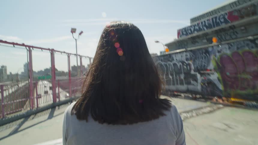 View of a woman with black hair walking on an overpass through a city during the day