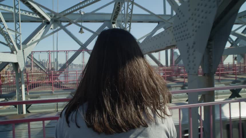 Point of view of a blackhaired woman on an overpass next to a passing train