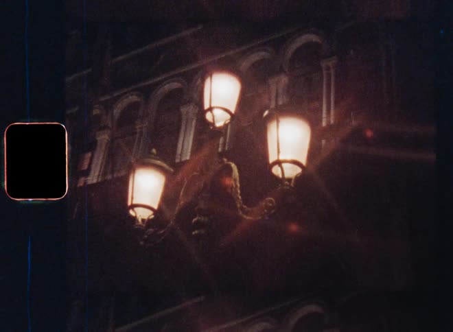 Bright warm street lighting or streetlamps on a pole next to an old building with pillars and windows at night shine onto the road in a village or city illuminating the pavement or sidewalk