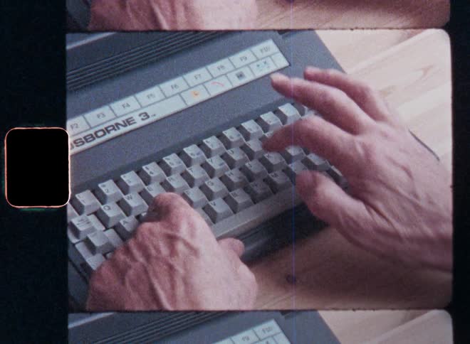 Handheld Super-8 film footage of the hands of an old man typing on a vintage laptop PC keyboard as he is pressing multiple keys with his fingers while programming or coding a computer program or writing an email as form of digital communication