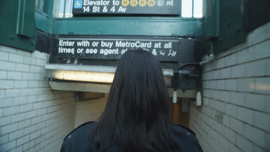 Back view of a woman with black hair descending into a tunnel at a train station