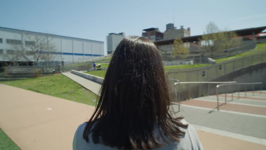 Point of view of a blackhaired woman walking on artificial grass towards a hallway with buildings around her