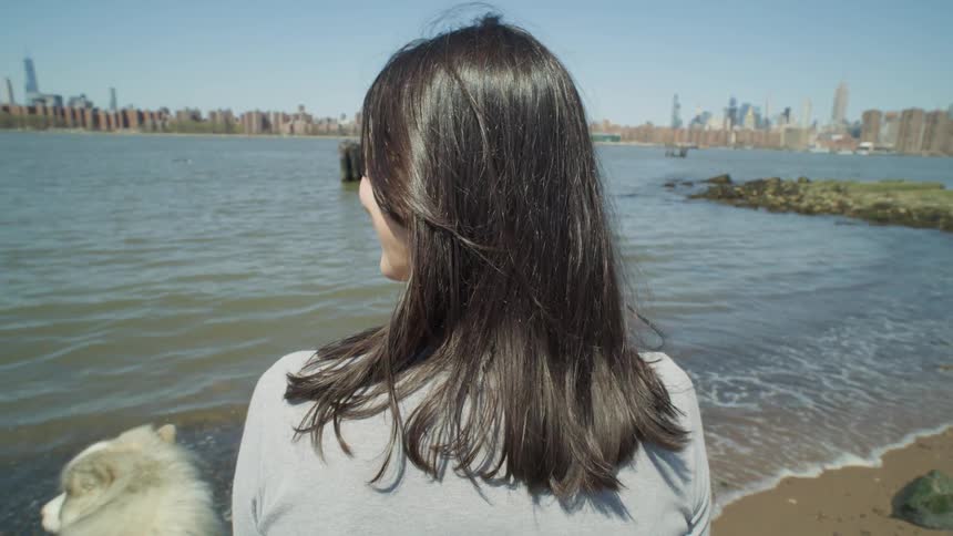 A woman walking on the beach with a view of the NYC skyline