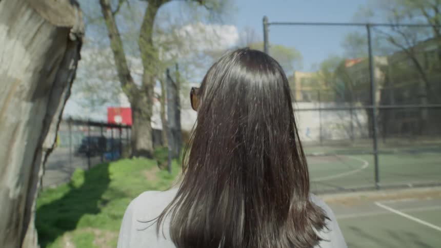 Black haired woman seen from behind walking by outdoor sports courts in NYC
