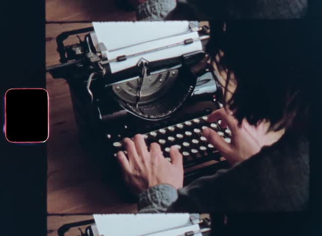 Unrecognisable woman or man with long hair wearing gray shirt sitting at wooden desk or table uses an old vintage typewriter to write or type a letter or story essay or newspaper article in the 1970s or 1980s before the digital age